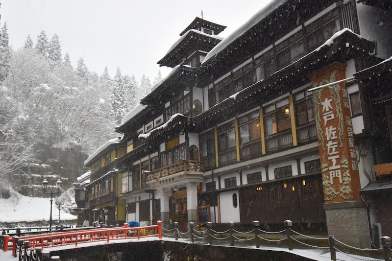 A tall wooden inn front with balconies and plaster panels beside a narrow river.