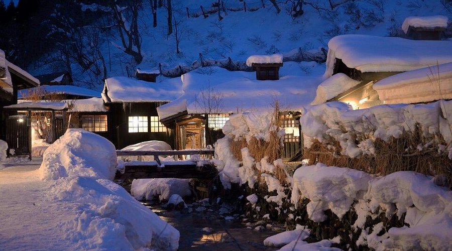 A long low timber building with a shingled roof under deep snow.