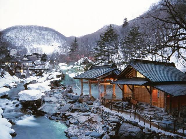 Timber lodging buildings on both banks of a mountain river joined by a footbridge.
